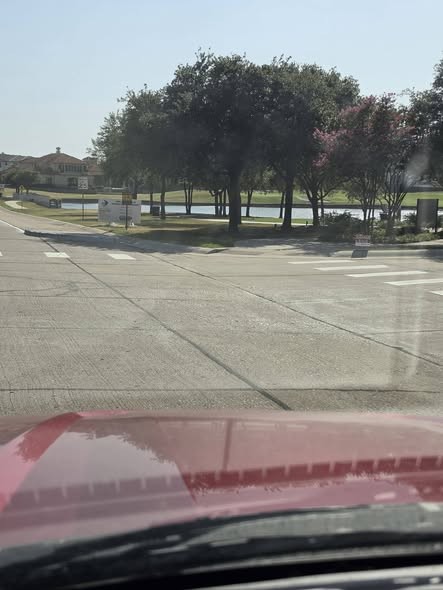Driver-eye view of a King Arthur intersection where concrete bump-outs sit partly in tree shadow